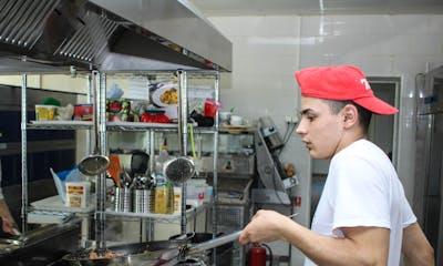 A young man working in a professional kitchen, cooking with a frying pan.