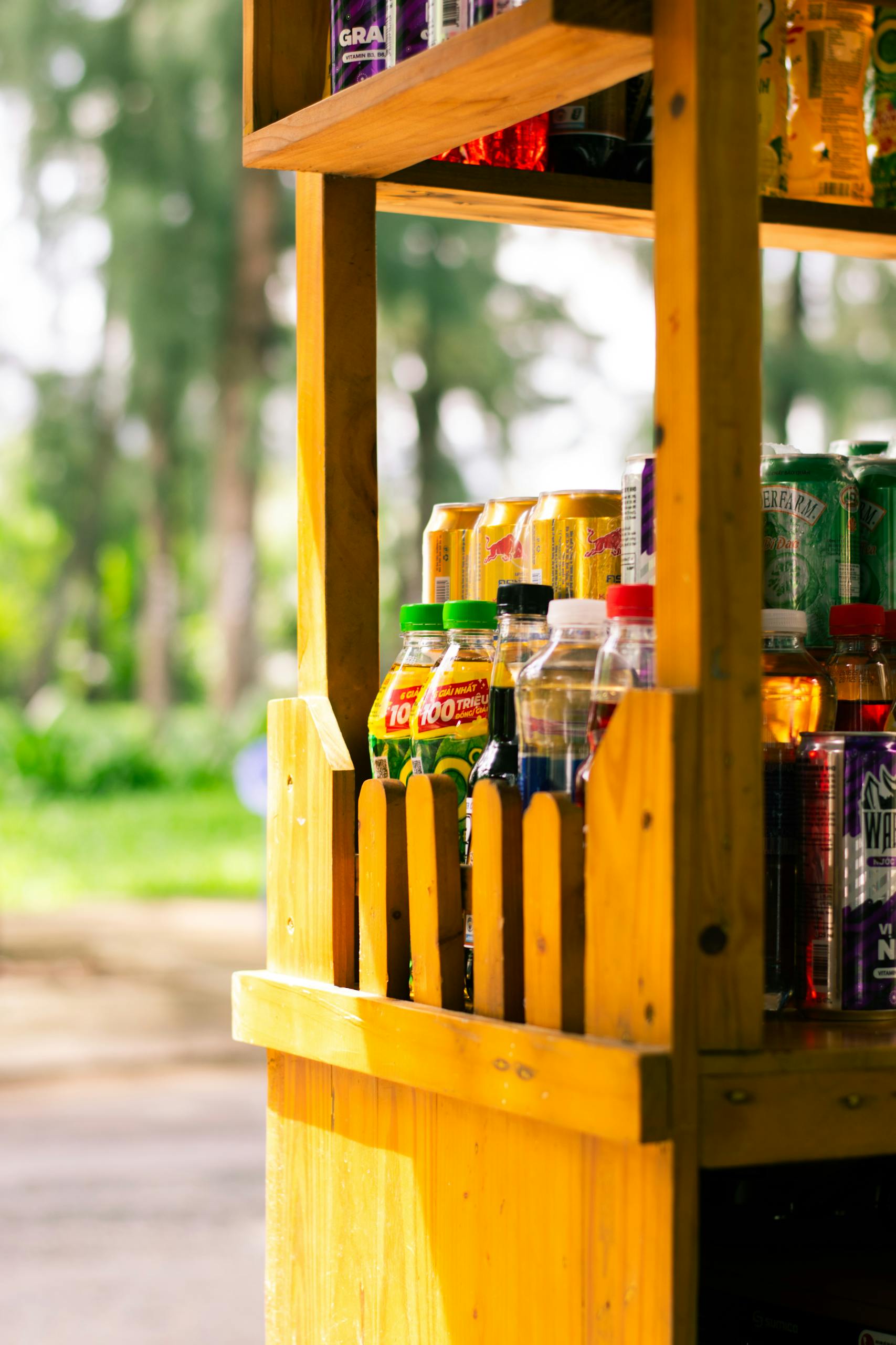 Vibrant wooden beverage stand with colorful bottles in a sunny outdoor setting.